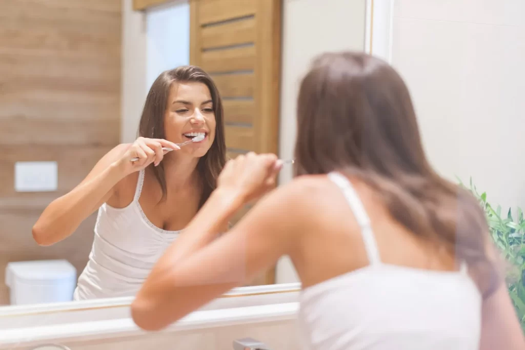 Woman brushing teeth at home to illustrate daily care habits that help veneers stay in good condition for many years.