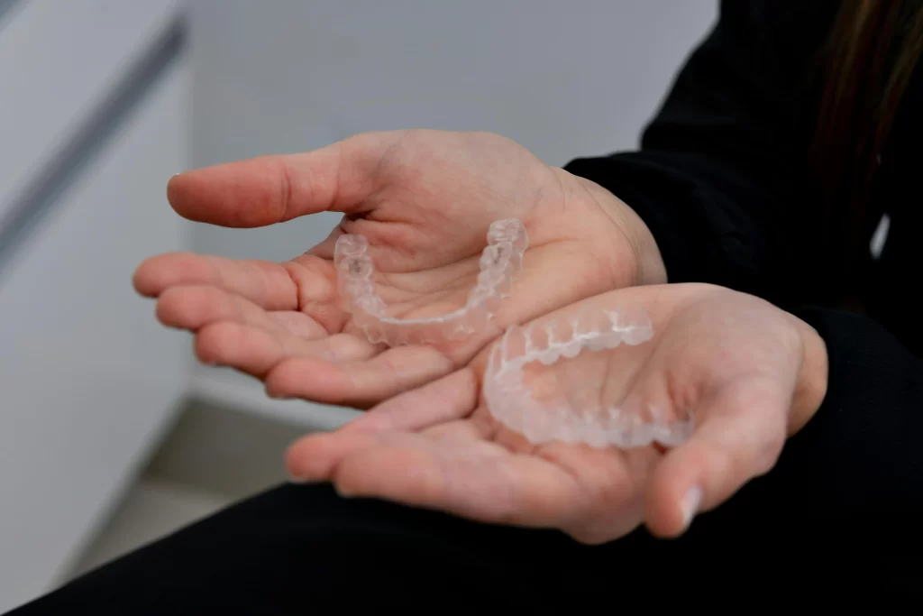 Close-up of hands holding two clear aligner trays used during Invisalign treatment.