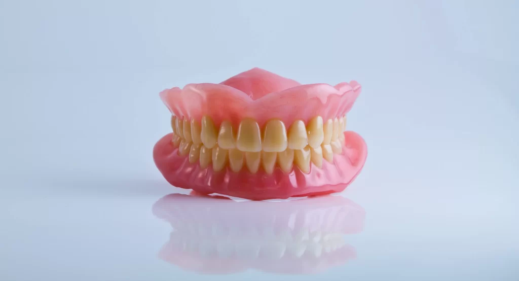 Full set of upper and lower acrylic dentures on a clean surface against a light background.